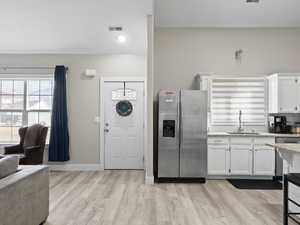 Kitchen featuring stainless steel refrigerator with ice dispenser, light hardwood / wood-style floors, sink, and white cabinets