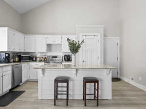 Kitchen featuring a center island, appliances with stainless steel finishes, light stone countertops, and high vaulted ceiling