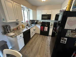 Kitchen with sink, white cabinets, light hardwood / wood-style floors, and black appliances