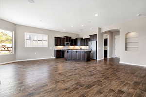 Kitchen with dark brown cabinets, a center island with sink, dark hardwood / wood-style flooring, stainless steel appliances, and decorative backsplash