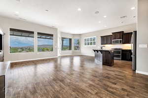 Kitchen with dark hardwood / wood-style floors, stainless steel appliances, a kitchen breakfast bar, and an island with sink