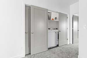 Clothes washing area featuring light colored carpet and washing machine and dryer