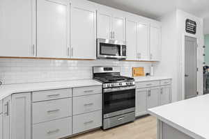 Kitchen featuring backsplash, stainless steel appliances, light hardwood / wood-style floors, and white cabinets