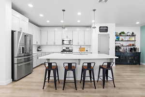 Kitchen with sink, decorative light fixtures, appliances with stainless steel finishes, a kitchen island with sink, and white cabinets