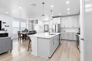 Kitchen with sink, appliances with stainless steel finishes, a kitchen breakfast bar, an island with sink, and decorative light fixtures