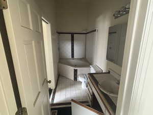 Bathroom featuring tile patterned flooring, tiled tub, vanity, and toilet