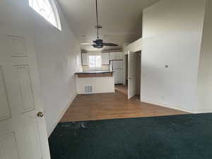 Kitchen featuring kitchen peninsula, white fridge, hardwood / wood-style flooring, ceiling fan, and white cabinets