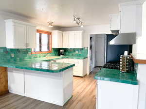 Kitchen with white cabinetry, light wood-type flooring, tile counters, kitchen peninsula, and decorative backsplash