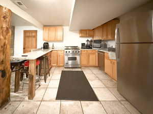 Kitchen featuring stainless steel appliances, light tile patterned flooring, light brown cabinets, and kitchen peninsula