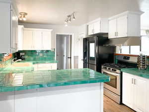 Kitchen featuring white cabinetry, sink, tile counters, kitchen peninsula, and stainless steel appliances