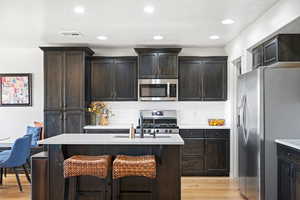 Kitchen featuring light hardwood / wood-style flooring, dark brown cabinets, stainless steel appliances, and a kitchen breakfast bar