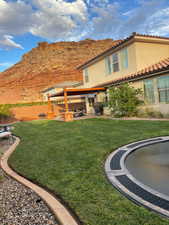 Rear view of house with a trampoline, a mountain view, a lawn, and a patio area