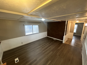 Spare room featuring dark wood-type flooring, a textured ceiling, and beam ceiling