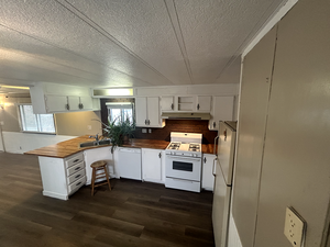 Kitchen featuring white cabinetry, white appliances, dark hardwood / wood-style flooring, and kitchen peninsula