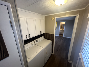 Washroom featuring dark wood-type flooring, washer and clothes dryer, cabinets, and a textured ceiling