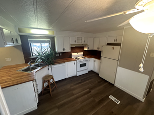 Kitchen featuring white cabinetry, butcher block counters, sink, dark wood-type flooring, and white appliances