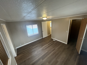 Unfurnished bedroom featuring crown molding, dark hardwood / wood-style floors, and a textured ceiling