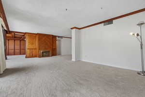 Unfurnished living room featuring crown molding, light colored carpet, and a textured ceiling