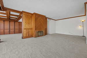 Unfurnished living room featuring crown molding, light carpet, and a textured ceiling