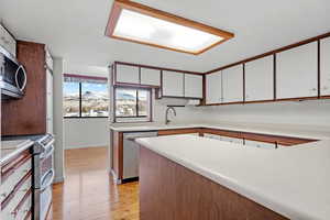 Kitchen featuring stainless steel appliances, sink, light wood-type flooring, and white cabinets