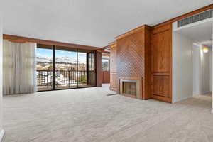 Unfurnished living room with floor to ceiling windows, wooden walls, light carpet, and a textured ceiling