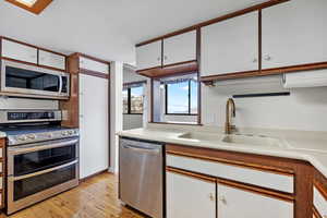 Kitchen with white cabinetry, stainless steel appliances, sink, and light hardwood / wood-style flooring