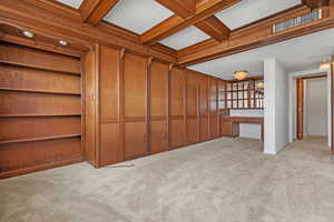 Interior space featuring beamed ceiling, built in desk, light carpet, and wood walls