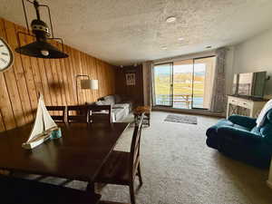 Carpeted dining area with wood walls and a textured ceiling
