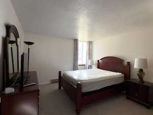 Bedroom with a baseboard heating unit, a textured ceiling, and carpet