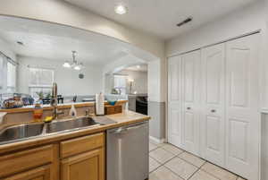 Kitchen featuring dishwasher, sink, hanging light fixtures, light tile patterned floors, and an inviting chandelier