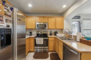 Kitchen featuring stainless steel appliances, sink, light tile patterned floors, and kitchen peninsula