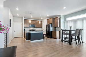 Kitchen with large island, pendant lights, light wood-type laminate flooring, a kitchen breakfast bar, and black stainless-steel appliances