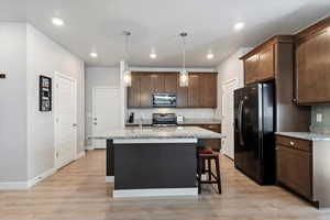 Kitchen featuring black stainless-steel appliances, a kitchen island with single basin sink, granite countertops, and pendant lights