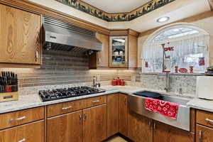 Kitchen featuring tasteful backsplash, light stone counters, exhaust hood, and black gas cooktop