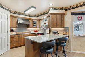 Kitchen with backsplash, black electric stovetop, kitchen peninsula, a kitchen bar, and exhaust hood