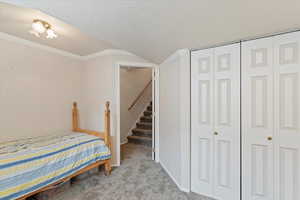 Bedroom featuring ornamental molding, light colored carpet, a textured ceiling, and a closet