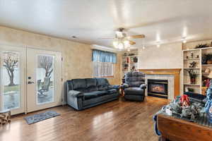 Living room featuring hardwood / wood-style flooring, ceiling fan, a fireplace, and a textured ceiling