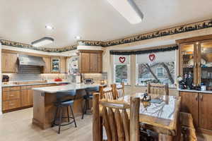 Kitchen featuring backsplash, light hardwood / wood-style floors, wall chimney exhaust hood, and a kitchen bar