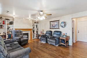 Living room with track lighting, ceiling fan, wood-type flooring, and a tiled fireplace