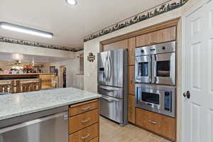 Kitchen with light stone counters, light hardwood / wood-style flooring, ceiling fan, and appliances with stainless steel finishes