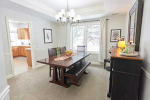 Dining space with crown molding, light colored carpet, a chandelier, and a tray ceiling