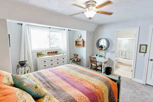 Bedroom with lofted ceiling, ensuite bath, light colored carpet, a textured ceiling, and ceiling fan