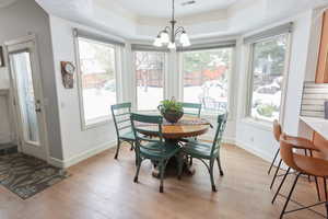 Dining area with crown molding, a notable chandelier, light hardwood / wood-style floors, and a tray ceiling