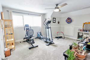 Exercise area featuring ceiling fan, carpet floors, and a textured ceiling