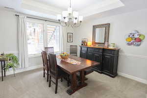 Carpeted dining room with a notable chandelier, a tray ceiling, and ornamental molding