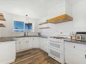 Kitchen with decorative light fixtures, sink, white cabinets, custom range hood, and white appliances