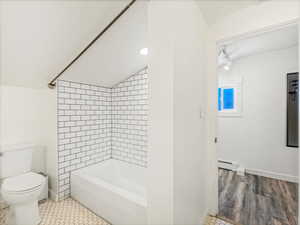 Bathroom featuring baseboard heating, tile patterned flooring, tiled shower / bath combo, vaulted ceiling, and toilet