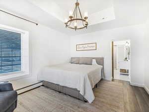 Bedroom with an inviting chandelier, wood-type flooring, a tray ceiling, and a baseboard heating unit