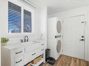 Laundry room with sink, hardwood / wood-style flooring, cabinets, and stacked washer / dryer