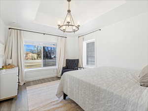 Bedroom with hardwood / wood-style flooring, a tray ceiling, and a chandelier